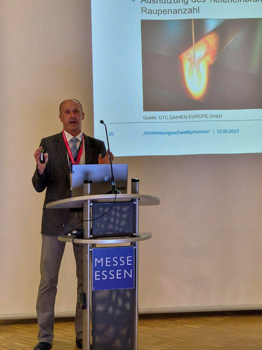 Mann im schwarzen Anzug steht vor Rednerpult der Messe Essen, im Hintergrund ist eine Präsentationsfolie, die einen Schmelzprozess zeigt.