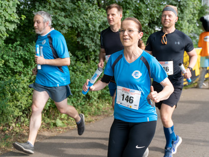 Vier Personen beim Lauf auf einem Waldweg, drei Männer und eine Frau tragen Sportkleidung und Startnummern, zwei in SLV-Halle-Trikots mit Staffelstäben in der Hand