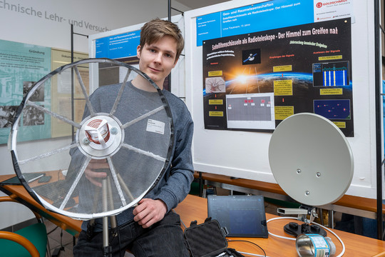 Ein junger Mann hält eine selbstgebaute Satellitenantenne aus Metall und Netzgewebe.
