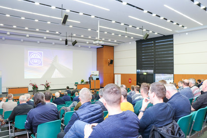 Publikum verfolgt im Hörsaal der SLV Halle einen Fachvortrag zum Thema Brückenbau, auf der Leinwand ist eine Brückenkonstruktion mit Veranstaltungssymbol zu sehen.
