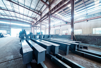 Große Industriehalle mit gestapelten Metallträgern und einfallendem Tageslicht