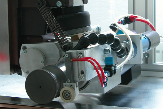 Ein präzisionsgeführtes industrielles Gerät mit mehreren flexiblen Schläuchen, Druckfedern und Rollen ist auf einer Metalloberfläche montiert. Es handelt sich um eine automatisierte Vorrichtung zur Oberflächenbearbeitung oder Nahtverfolgung.