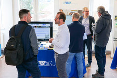 Mehrere Personen stehen an einem Informationsstand der SLV Halle GmbH mit Monitor und tauschen sich über Inhalte aus