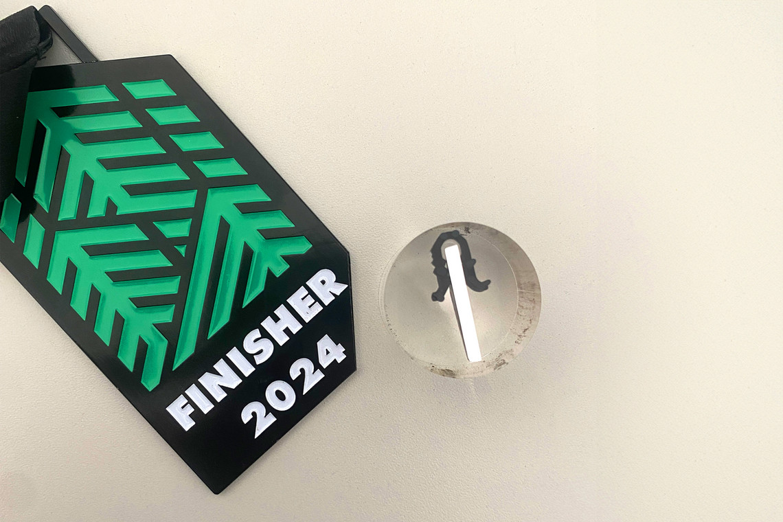 Medaille mit Aufdruck "Finisher 2024", abgeschnittenes Stück ist im Mikroschliff eingefasst