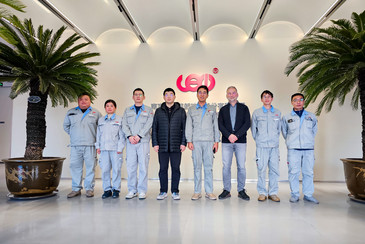 Mehrere Personen stehen in einer offenen Eingangshalle mit Glasfront und Palmen.