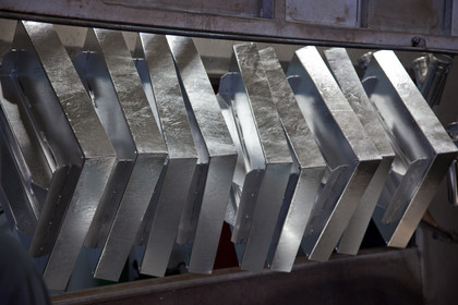 Metallteile nach dem Feuerverzinken hängen nebeneinander in einer Verzinkungsanlage