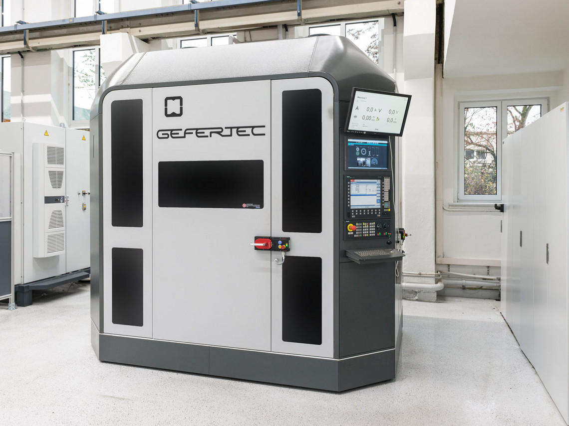 Geschlossenes 3D-Drucksystem in Industrieumgebung mit integriertem Display, Bedienfeld und Sichtfenster zur Überwachung des Bauprozesses. Das Gehäuse ist in Grau gehalten, mit dem Logo von „Additive Industries“.