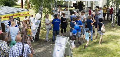 Zahlreiche Menschen besuchen bei sonnigem Wetter ein Sommerfest mit Informationsständen, Essensausgabe und Mitmachaktionen im grünen Außenbereich eines Instituts.