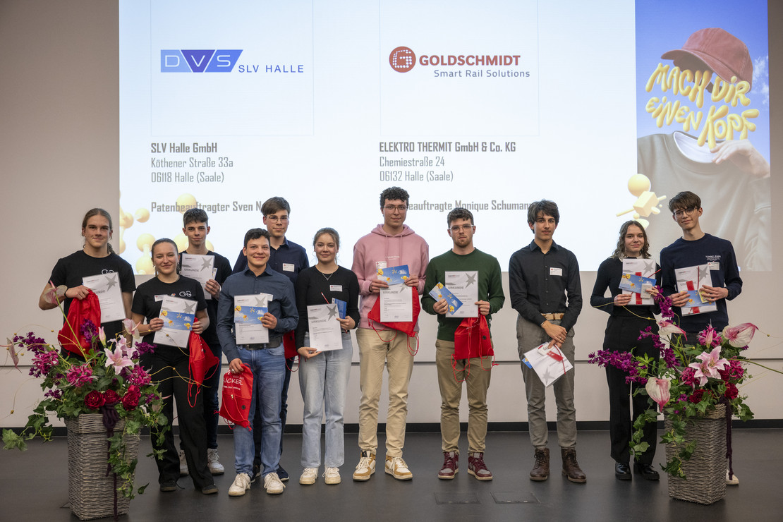 Eine Gruppe junger Menschen hält stolz ihre Urkunden und Geschenke auf einer Bühne mit SLV Halle-Logo. Hinter ihnen werden die Sponsoren und Veranstaltungspartner auf einer Leinwand angezeigt.