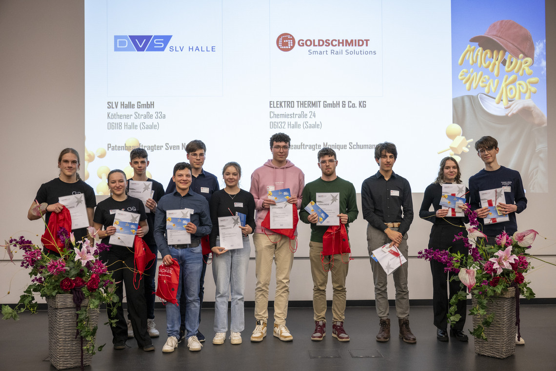 Eine Gruppe junger Menschen hält stolz ihre Urkunden und Geschenke auf einer Bühne mit SLV Halle-Logo. Hinter ihnen werden die Sponsoren und Veranstaltungspartner auf einer Leinwand angezeigt.