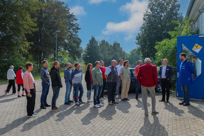 Besuchergruppe steht auf einem geräumigen Platz vor einer Werkhalle. 
