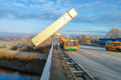 Lkw mit hochgeklapptem Auflieger steht quer auf einer Autobahnbrücke, weitere Fahrzeuge und ein orangefarbenes Baufahrzeug sind auf der vereisten Fahrbahn sichtbar.