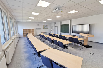 Großzügiger Tagungsraum geeignet für Präsentationen, mit Rednerpult, Beamer, Whiteboard, Tafel und leerem Regal für Materialien