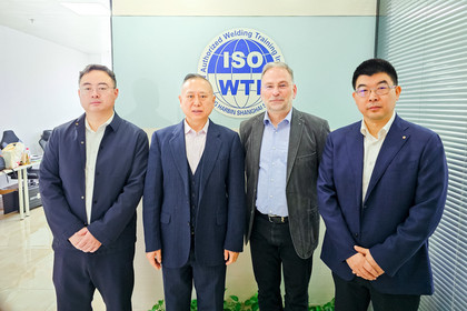 Vier Personen in Businesskleidung stehen nebeneinander vor einer Wand mit dem Schriftzug ISO WTI und blicken in die Kamera.