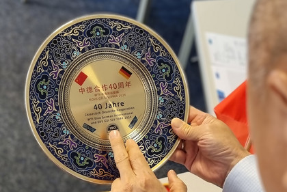 Ein Mann hält einen dekorativen Teller, der das 40-jährige Jubiläum der chinesisch-deutschen Kooperation feiert.