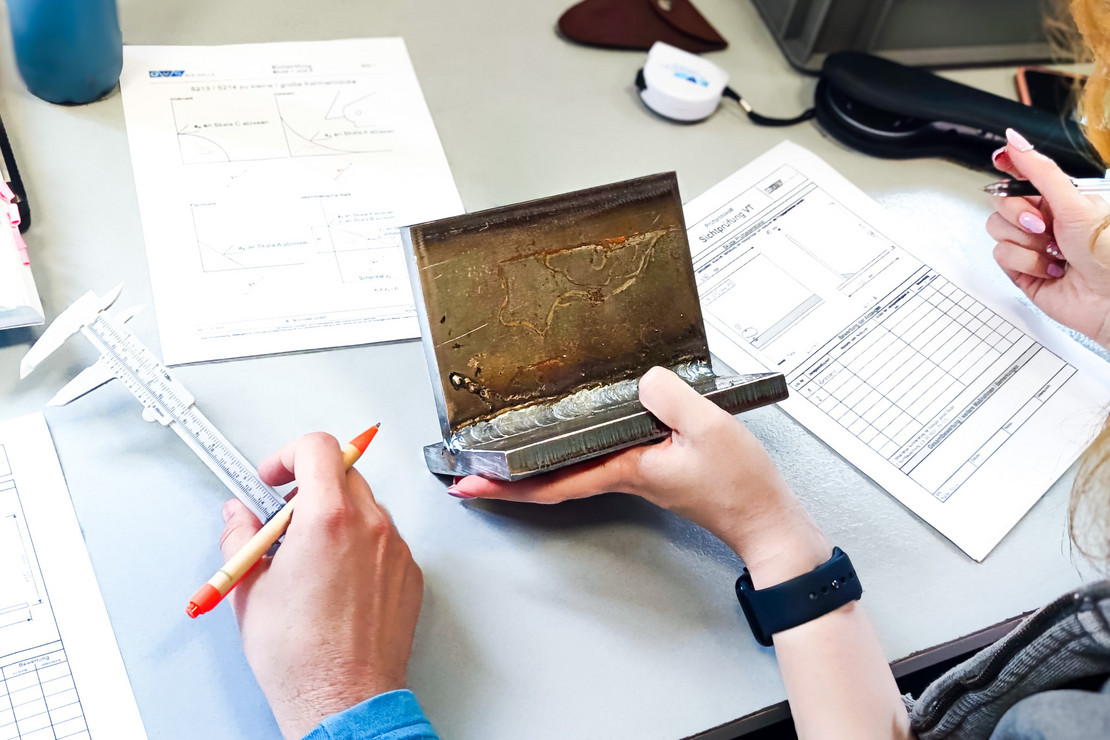 Zwei Personen arbeiten an einem Tisch mit technischen Zeichnungen und nehmen eine Sichtprüfung an einer Kehlnaht durch