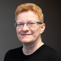 Anja Stückroth, im schwarzen Oberteil mit Brille, lächelnd vor neutralem Hintergrund