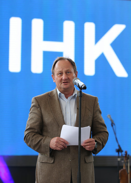 Mann im braunen Sakko spricht auf einer Bühne vor Mikrofon, hält ein Blatt Papier in der Hand, im Hintergrund große blaue Leinwand mit IHK-Schriftzug
