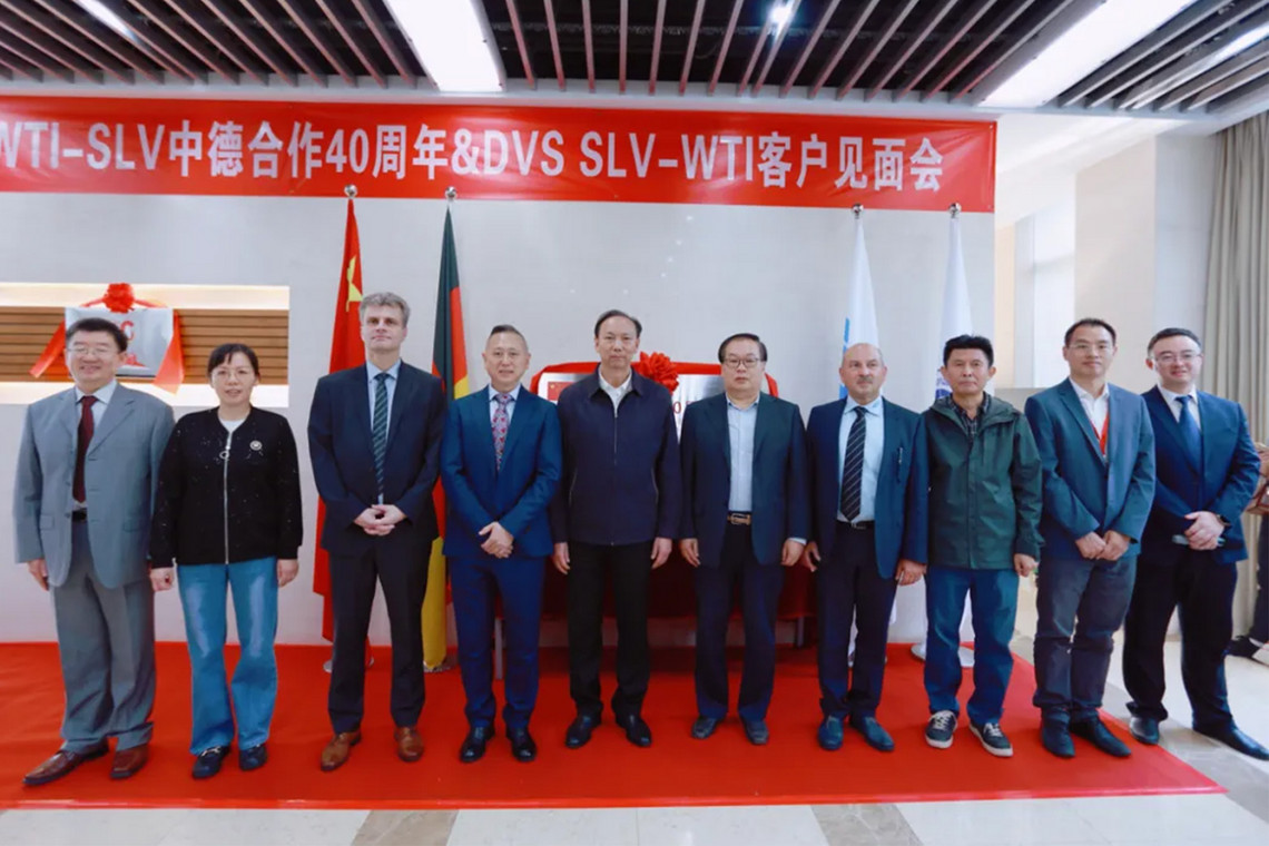 Eine Gruppe posiert für ein Foto vor Bannern und Flaggen, die auf die Veranstaltung in chinesischer Schrift hinweisen.
