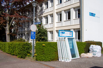 Stapel ausgebauter Fenster steht auf dem Gehweg vor dem Gebäude der SLV Halle, daneben ein großer Müllsack, im Hintergrund Büsche, Straßenschilder und ein Schild mit der Aufschrift „Haus 2“.