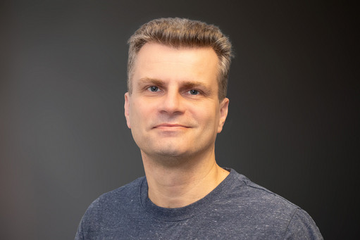 Steffen Wagner, im grauen Shirt, lächelnd vor neutralem Hintergrund