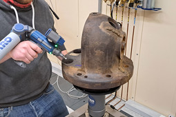 Eine Person scannt ein großes, rostiges Metallbauteil mit einem tragbaren 3D-Messarm in einem technischen Labor.