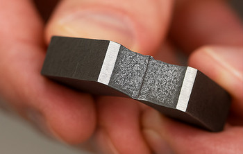 Hand hält ein metallisches Probestück nach einem Kerbschlagversuch