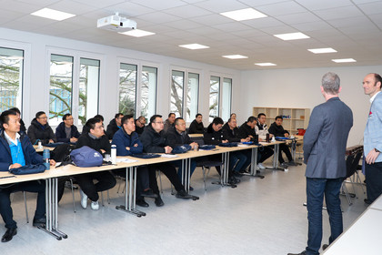 Schulungsteilnehmende folgen aufmerksam einer Präsentation im Seminarraum der SLV Halle. Zwei Mitarbeitende der SLV Halle stehen vorn und sprechen zur Gruppe.