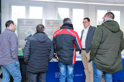 Austausch an einem Fachstand während der 33. Erfahrungsaustausch-Weiterbildung für Schweißaufsichtspersonen. Ein Experte erklärt vier Männern technische Lösungen für die Schweißtechnik.