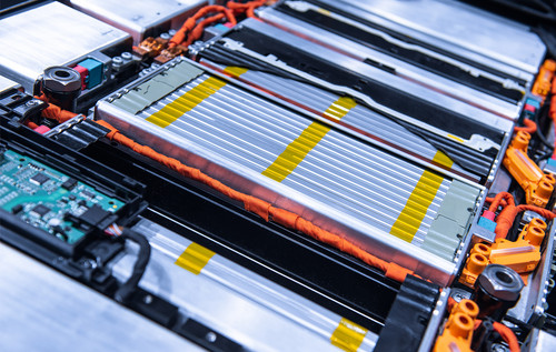 Detailansicht eines geöffneten Batteriepacks mit mehreren flachen Zellmodulen, orangefarbenen Hochvoltkabeln und elektronischen Steuerkomponenten.