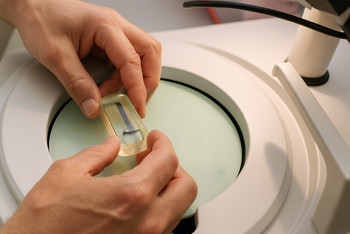 Hände platzieren eine kleine Probe auf einem Gerät zur metallografischen Schliff