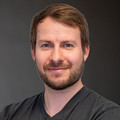 Amadeus Aurin, im schwarzen Shirt, lächelnd vor neutralem Hintergrund