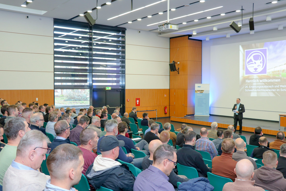 Großer Hörsaal mit zahlreichen Teilnehmenden, vorne hält eine Person einen Fachvortrag vor projizierter Präsentation, Publikum sitzt dicht beieinander und hört aufmerksam zu.