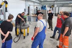 Eine Gruppe von Mitarbeitern beobachtet eine Vorführung zum induktiven Richten auf einem Metalltisch