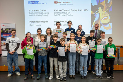 Gruppe von Kindern und Jugendlichen steht nebeneinander auf einer Bühne und hält Urkunden in die Kamera, im Hintergrund ist eine Präsentationsfolie mit Logos von SLV Halle GmbH und Elektrothermit projiziert.