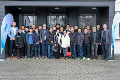 Gruppenfoto vor einem modernen Gebäudeeingang. Rechts und links stehen zwei Beachflags mit dem Firmenlogo der SLV Halle GmbH.