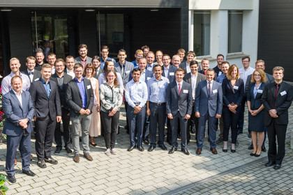 Gruppenfoto von 40 Personen in Businesskleidung vor einem Gebäude; darunter 33 Männer und 7 Frauen. Alle blicken in die Kamera und stehen auf einem gepflasterten Vorplatz.