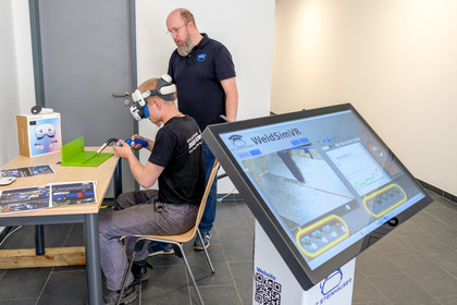 Teilnehmer mit VR-Brille beim virtuellen Schweißtraining mit WeldSimVR, betreut von einer Fachkraft, digitale Übungseinheit im Schulungsraum