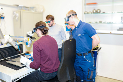 Ein Teilnehmer arbeitet mit Schutzbrille an einem Handschweißlaser, begleitet von anderen Teilnehmern, die den Prozess beobachten.