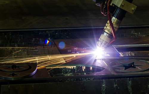Plasmaschneiden: Schweißbrenner erzeugt einen grellen Lichtbogen auf einer Metalloberfläche, Funken sprühen nach außen.
