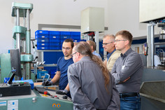 Besucher beobachten eine Live-Demonstration der zerstörungsfreien Prüfung von Betonstahl an einer Zug- und Druckprüfmaschine. 