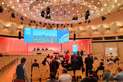 Teilnehmende betreten den Saal der DGZfP-Jahrestagung 2025 in Berlin, auf der großen Leinwand ist das Veranstaltungsdatum mit Berliner Stadtbild zu sehen; im Vordergrund leere und besetzte Stuhlreihen.