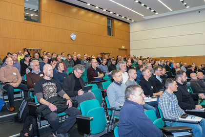 Viele Menschen sitzen aufmerksam im Auditorium, fast alle Stühle sind belegt