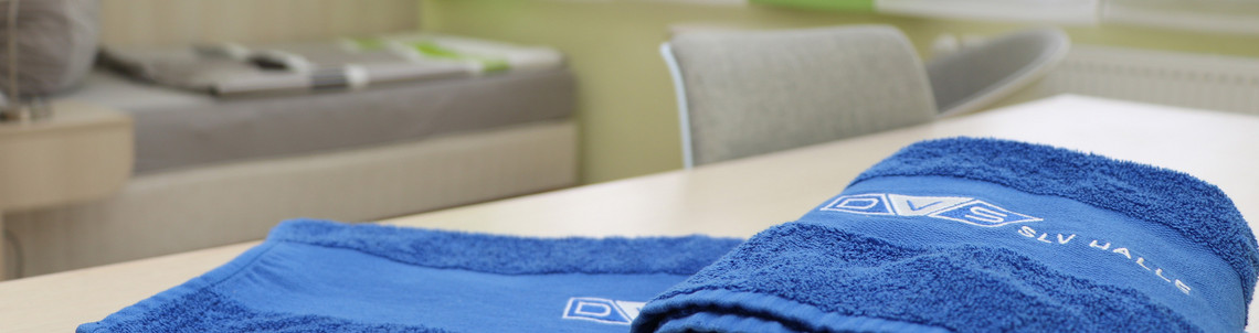 Nahaufnahme von zwei blauen Handtüchern mit dem Logo der SLV Halle auf einem Tisch in einem Einzelzimmer des Lerninternats.