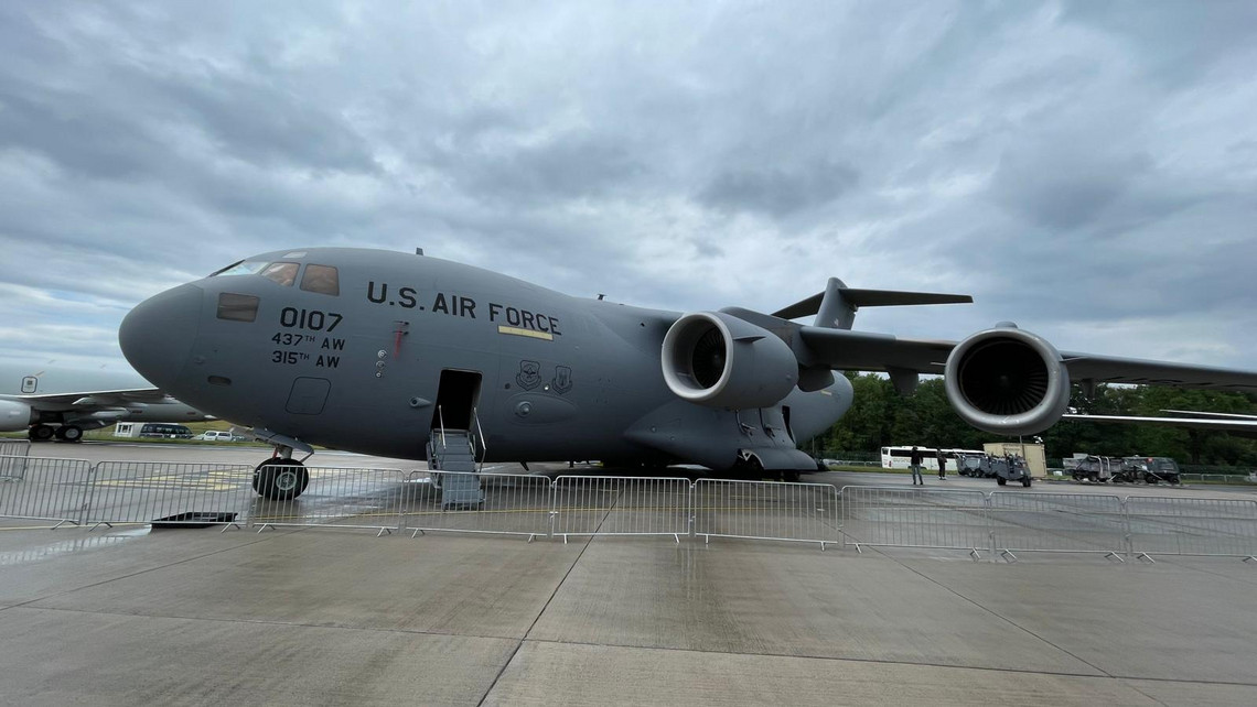 Großes Transportflugzeug der U.S. Air Force mit vier Triebwerken steht hinter einer Absperrung auf dem Rollfeld, Einstiegstreppe an der offenen Tür, grauer Himmel