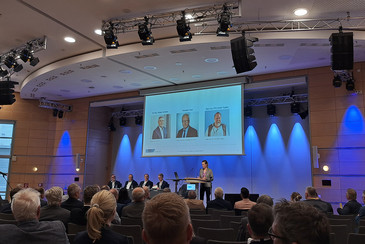 Podiumsdiskussion, im Hintergrund drei Portraits