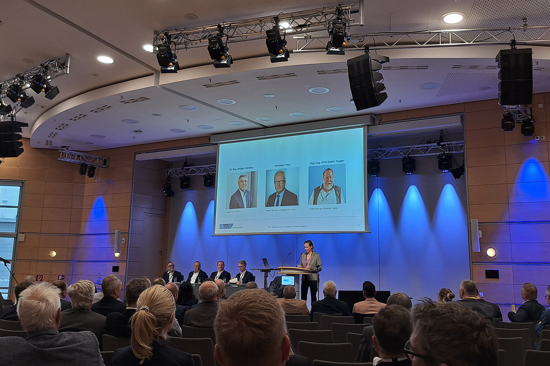 Podiumsdiskussion, im Hintergrund drei Portraits