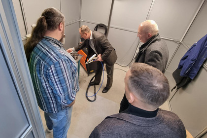 Fünf Männer und eine Frau beobachten die Präsentation des handgeführten Laserstrahlschweißens in einer Laserschutzkabine
