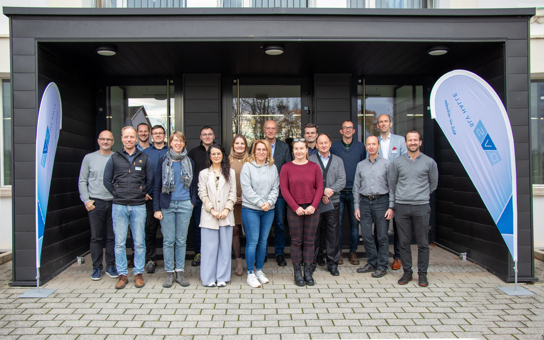 Gruppenfoto vor einem Eingangsbereich mit zwei DVS SLV Halle-Bannern, die Personen stehen auf einem gepflasterten Vorplatz und blicken freundlich in die Kamera.