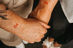 Zwei Frauen halten Hände, auf dem jeweiligen Handgelenk ist eine rote 224 tättowiert